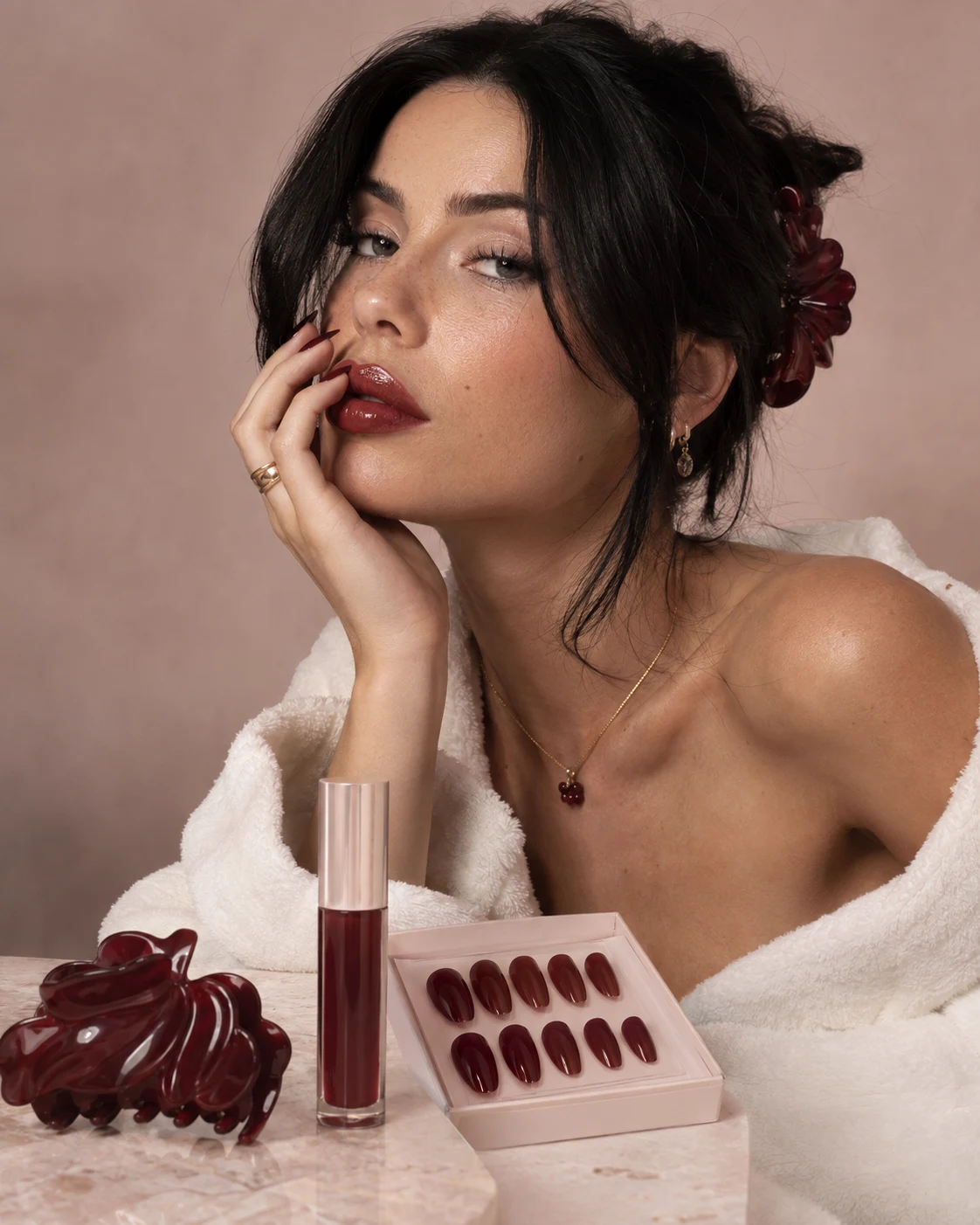 Model met diep wijnrode lippen en bijpassende press-on nagels, met een bordeauxrode klauwklem in haar haar