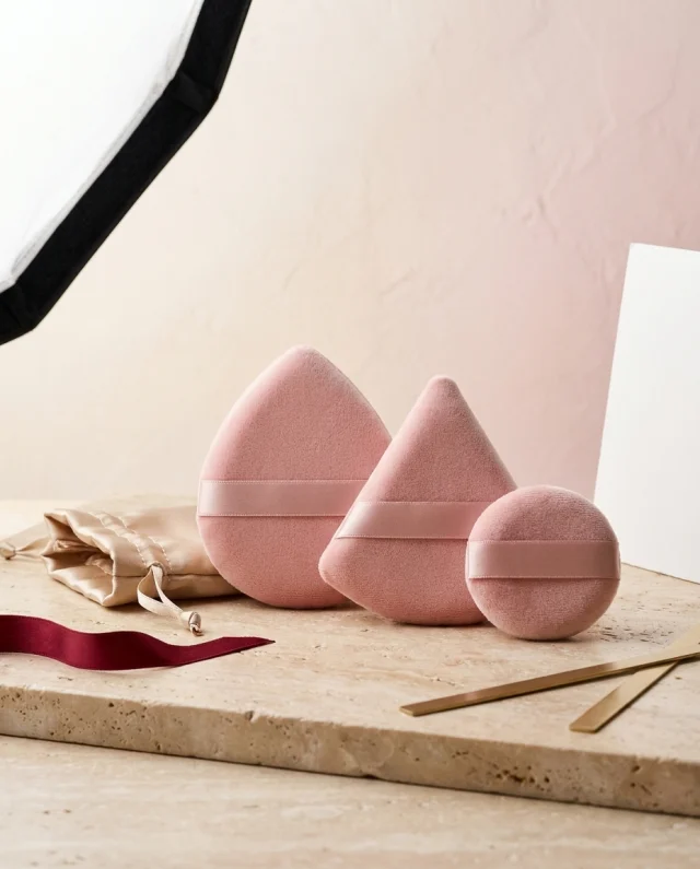 Drie velours poederdonsjes in ballet roze met satijnen zakje op een travertijnen plint