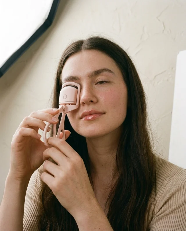 Vrouw houdt de verwarmde wimperkruller tegen haar bovenste wimpers