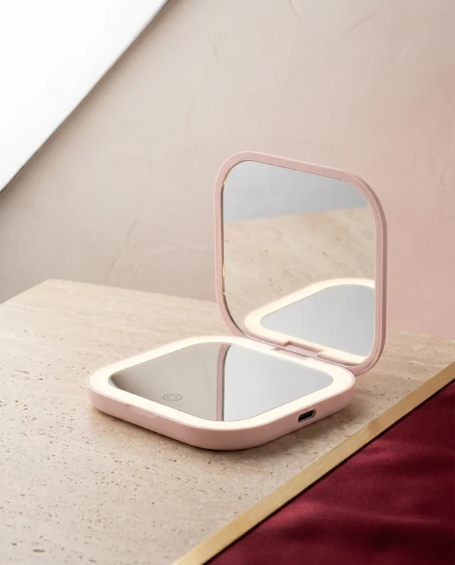 Opgevouwen LED-spiegel in blush roze, open en dicht, op een travertijnen plint