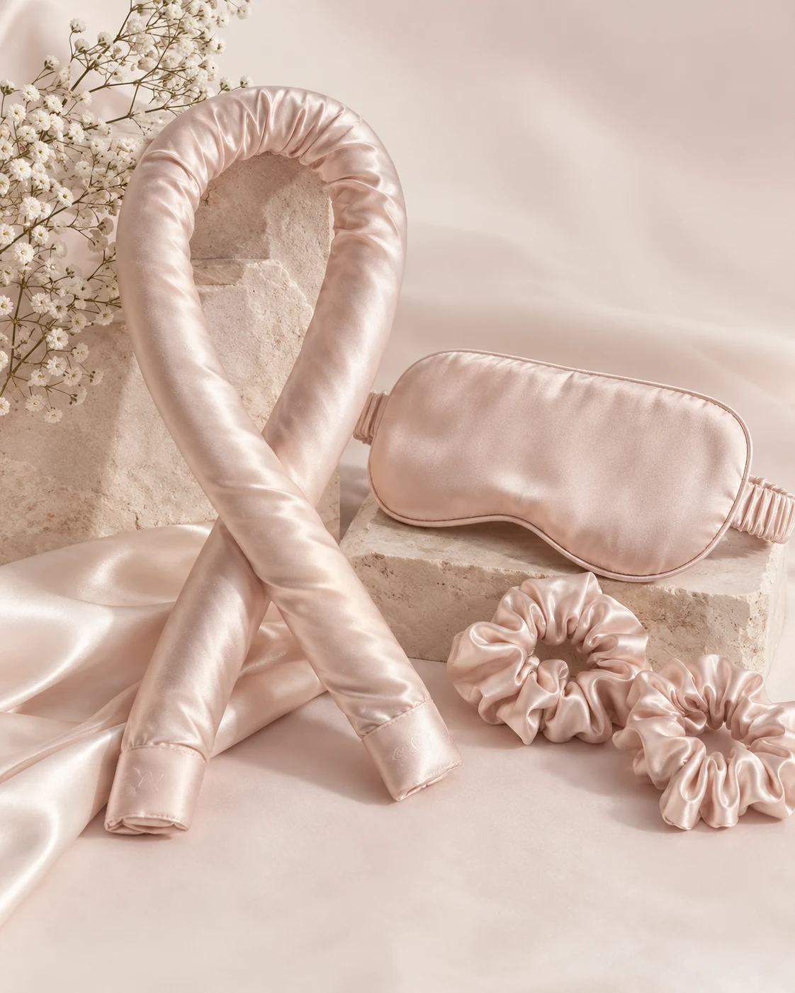 De Sleep Curl Kit in blush satijn: de krulrol, het slaapmasker en twee scrunchies op een zijden doek